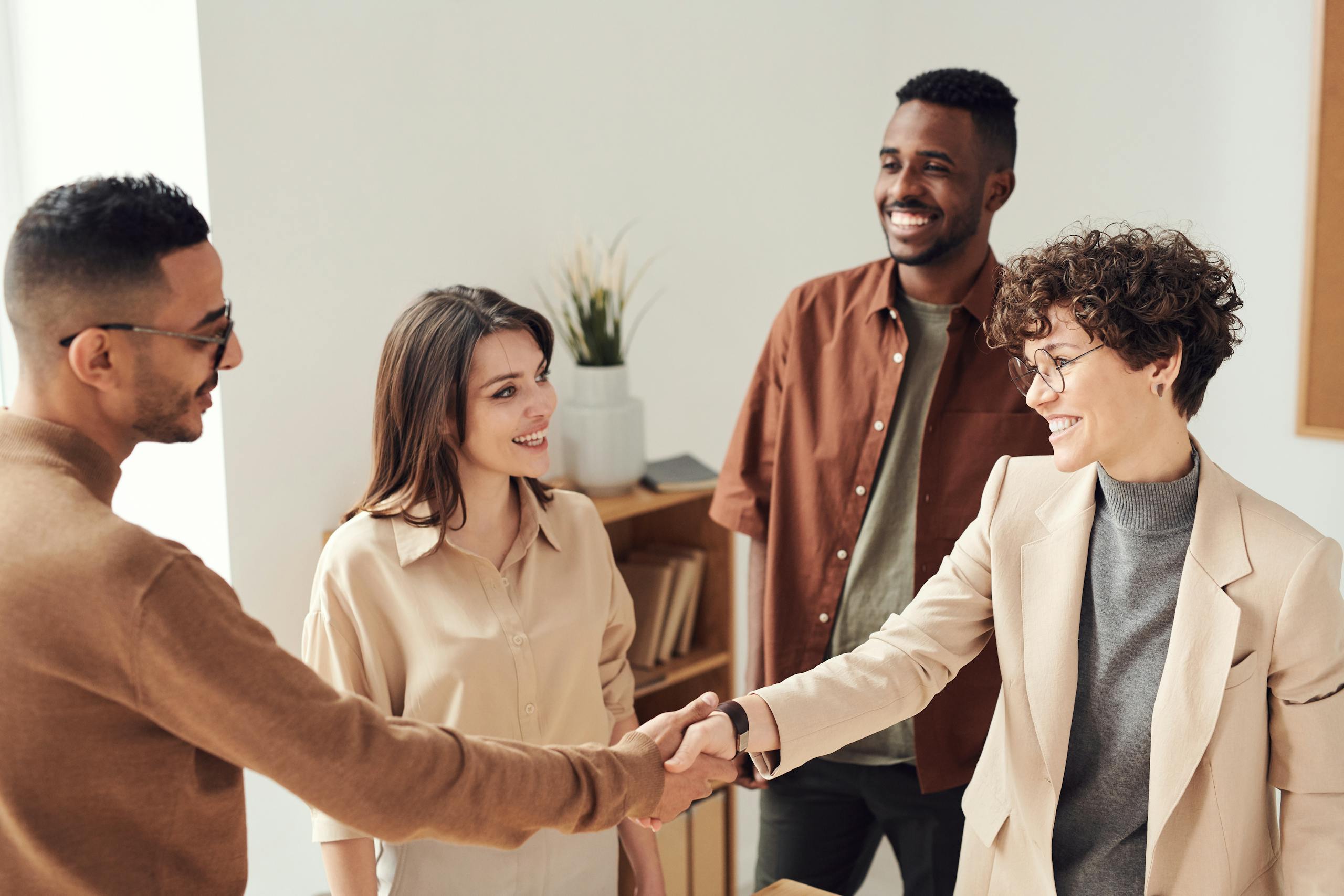 Four colleagues smiling and shaking hands in bright office setting.