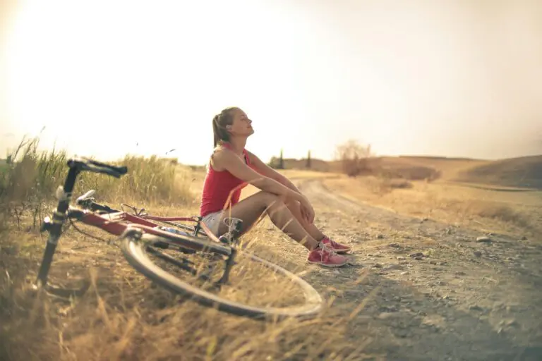 Woman sitting roadside in rural field with bicycle enjoying nature peacefully