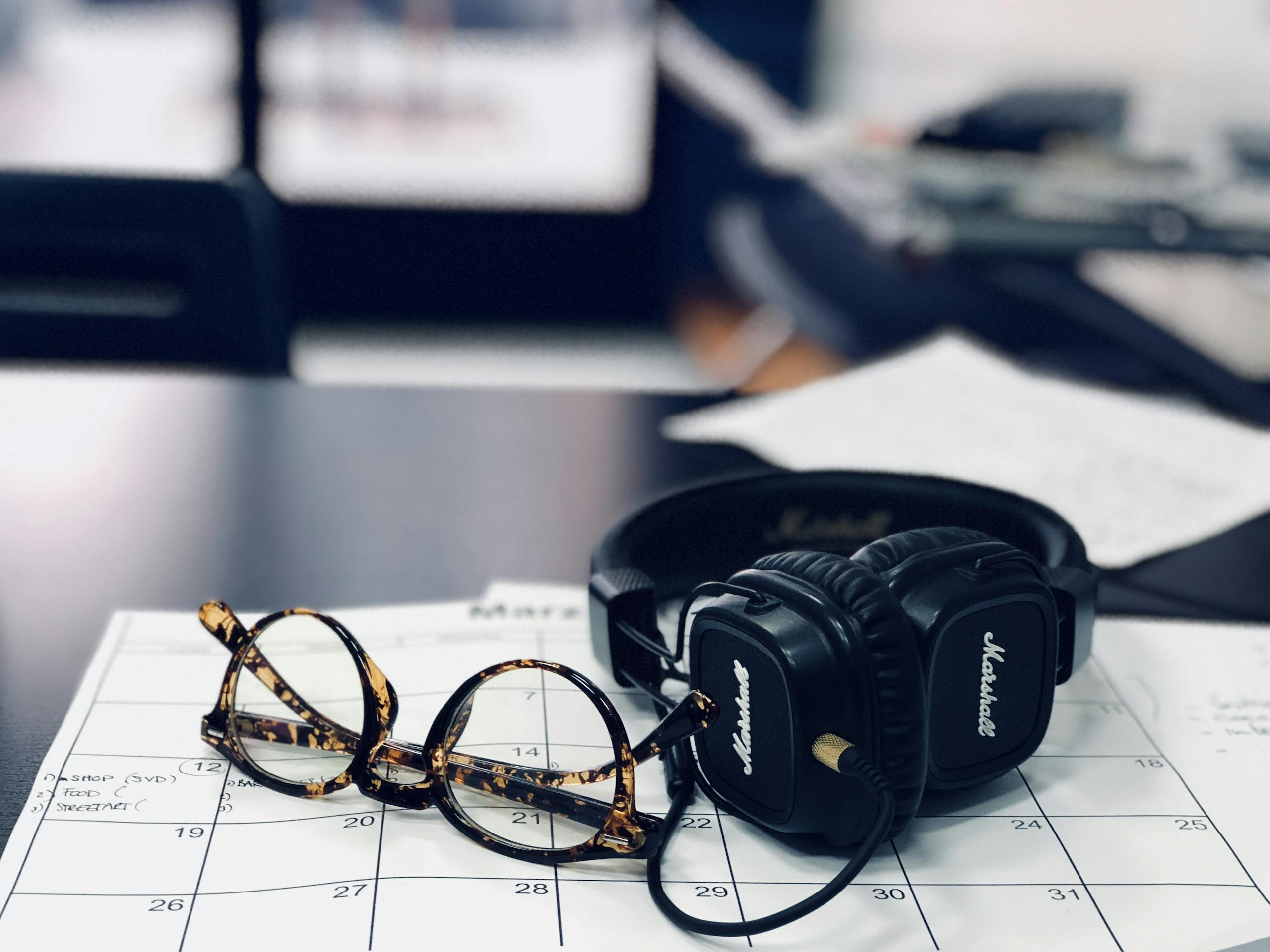 Glasses and headphones on desk calendar highlighting modern workspace essentials.