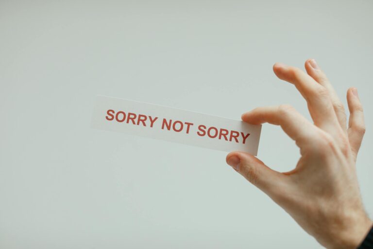 Hand holding card with phrase 'sorry not sorry' on neutral background.