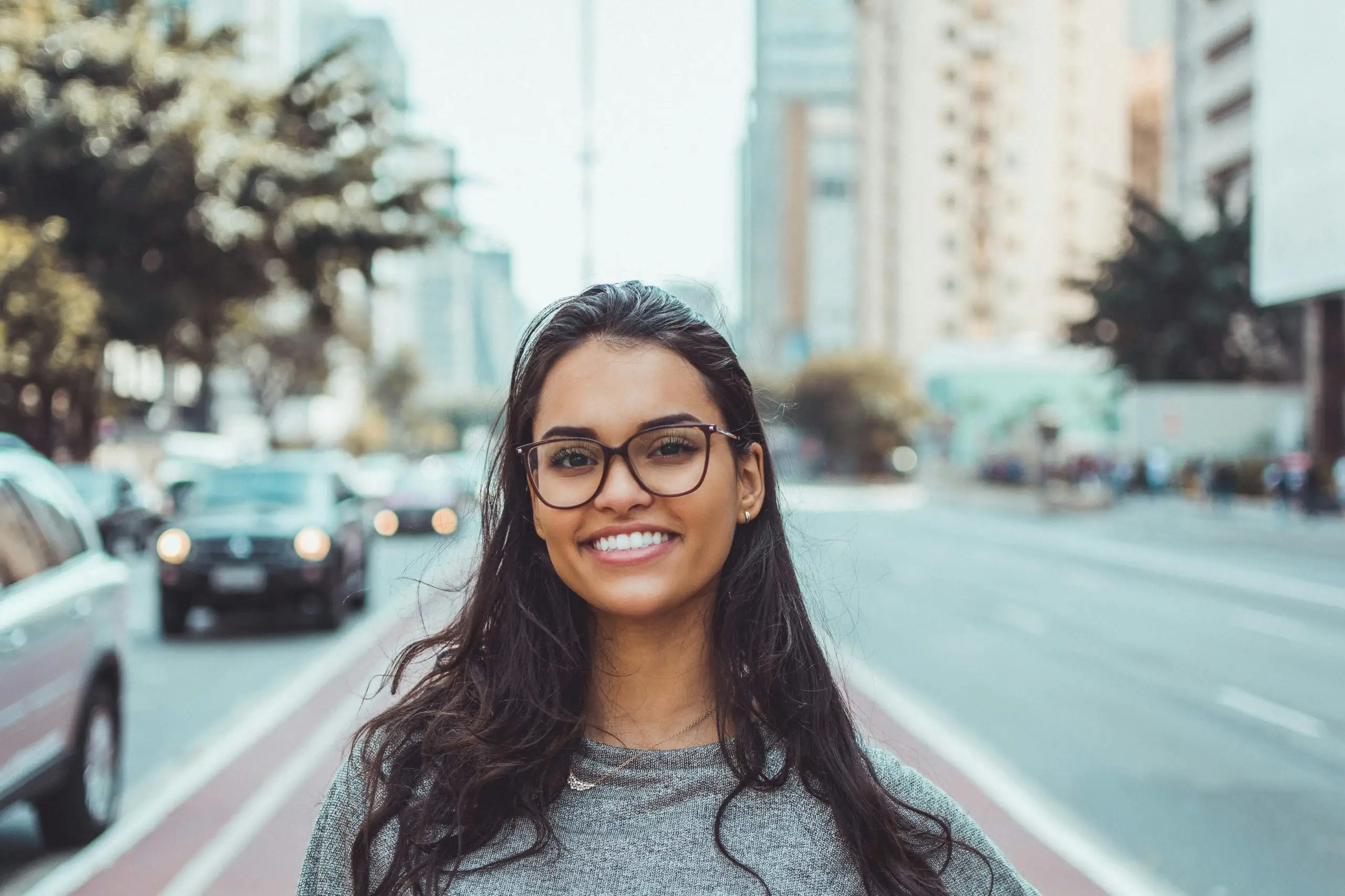 Young woman with glasses smiling confidently on urban city street