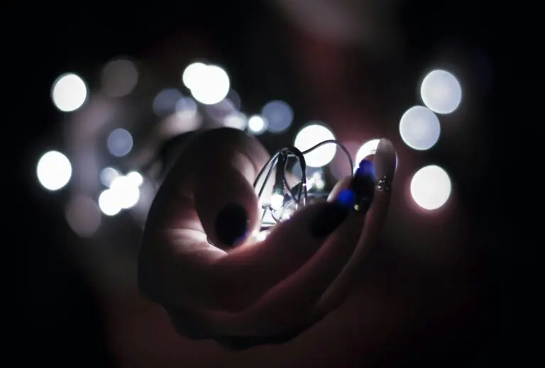 Hand holding glowing lightbulb surrounded by bokeh lights in darkness