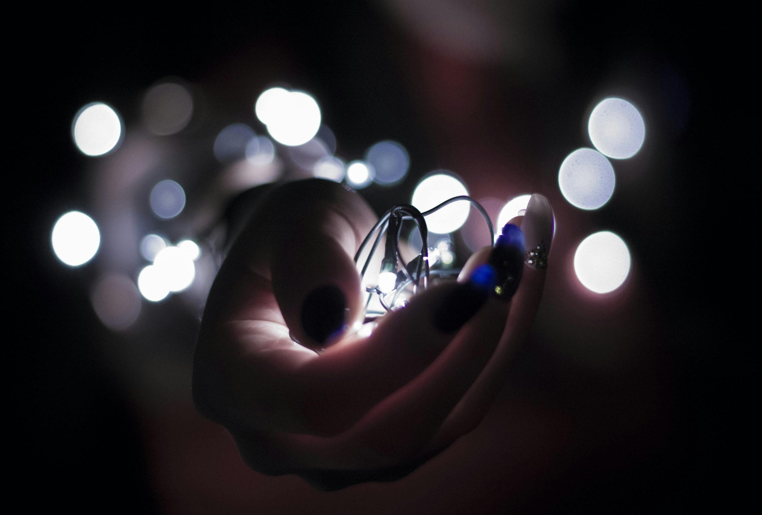 Hand holding glowing lightbulb surrounded by bokeh lights in darkness