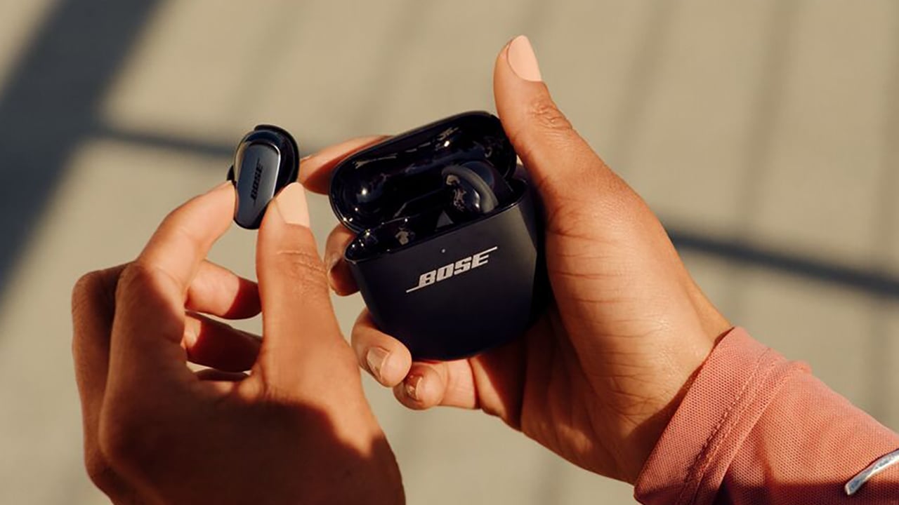 Person holding Bose earbuds and charging case in natural sunlight