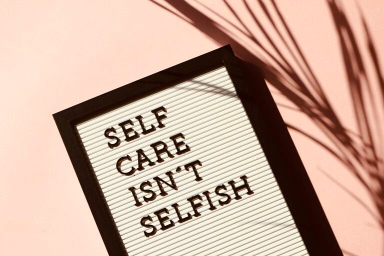 Letter board displaying self care quote with artistic shadow on pink background.