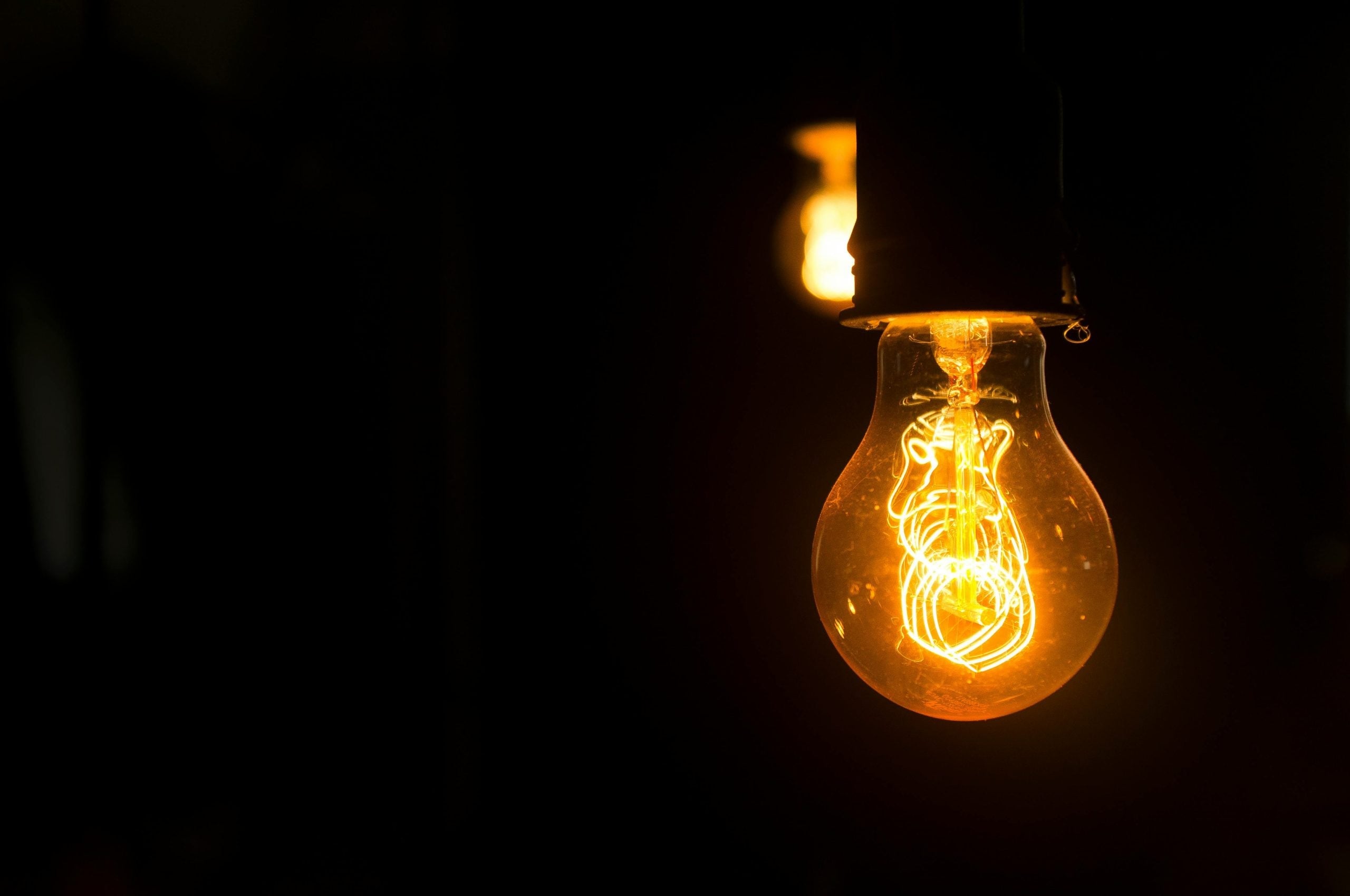 Glowing incandescent light bulb against dark background, filament brightly lit