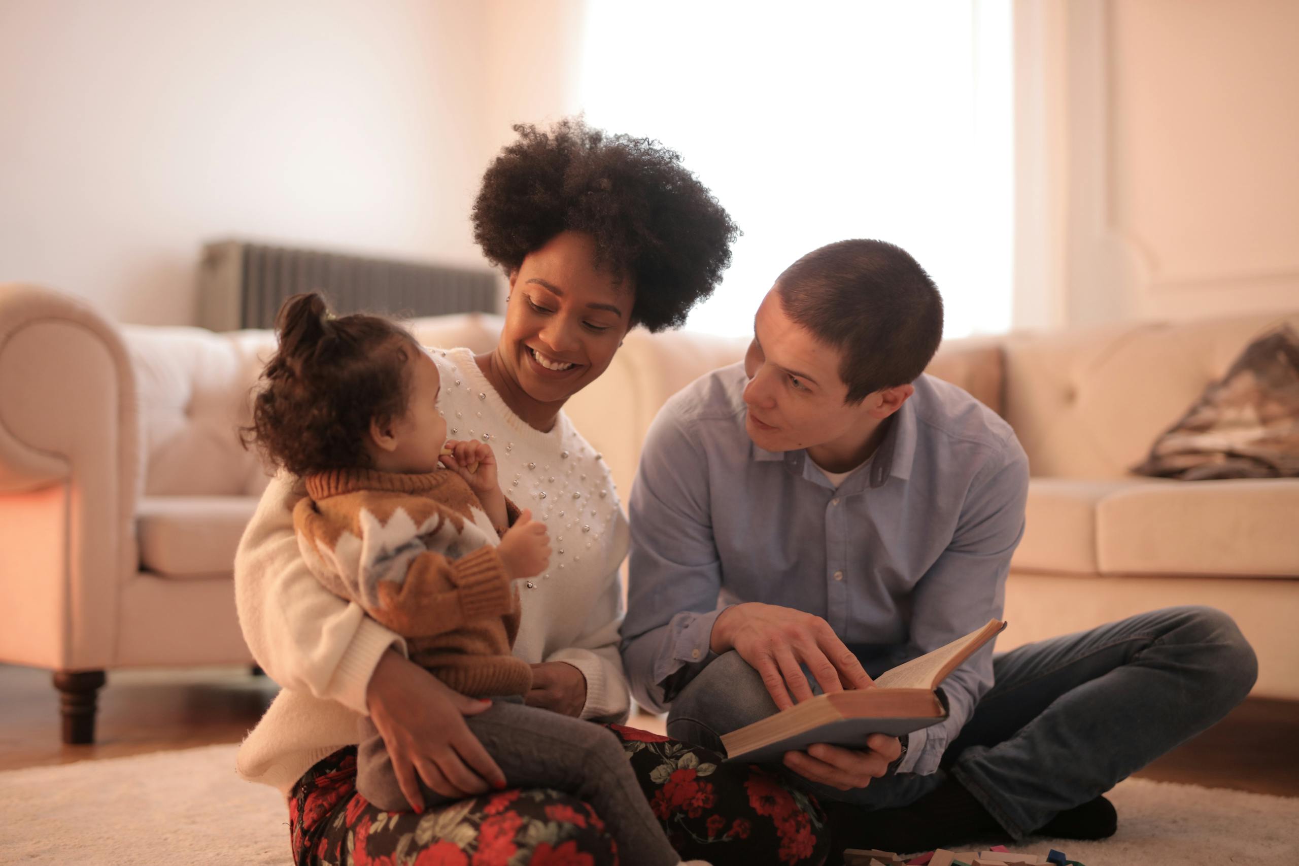 Loving parents reading with cheerful toddler in cozy living room