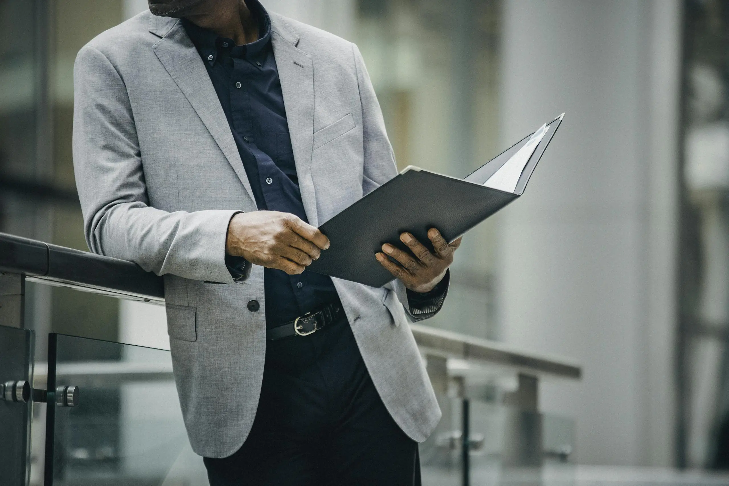 Man in suit reviews documents leaning on railing outdoors, professional and focused.