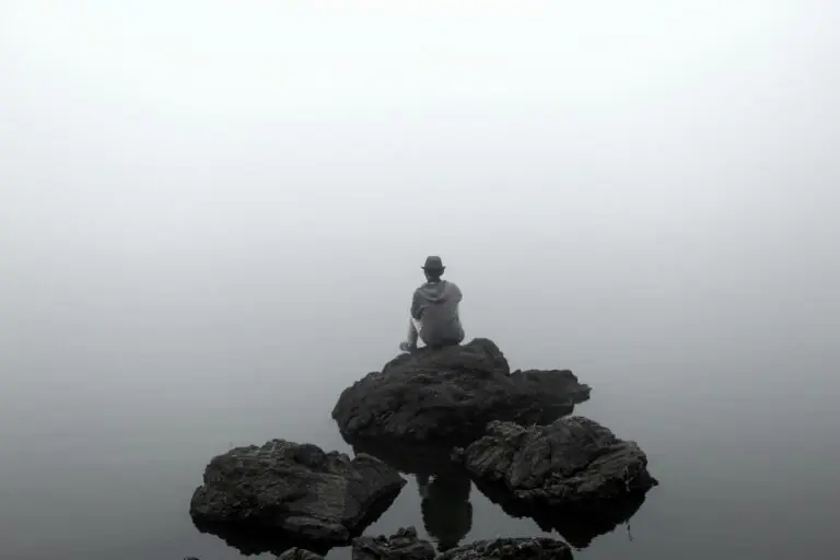 Man sitting on rock overlooking calm lake in nature