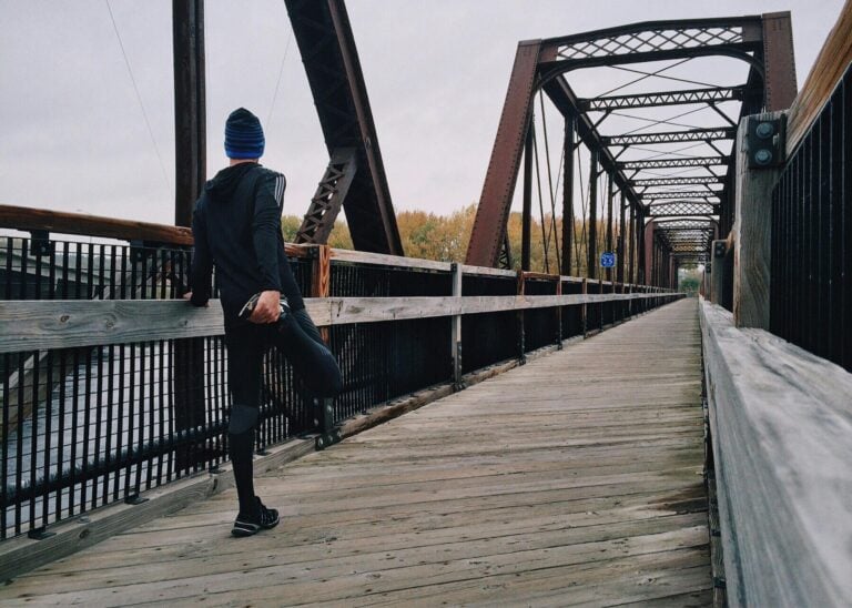 Man stretching on wooden footbridge during daytime run emphasizing fitness recreation