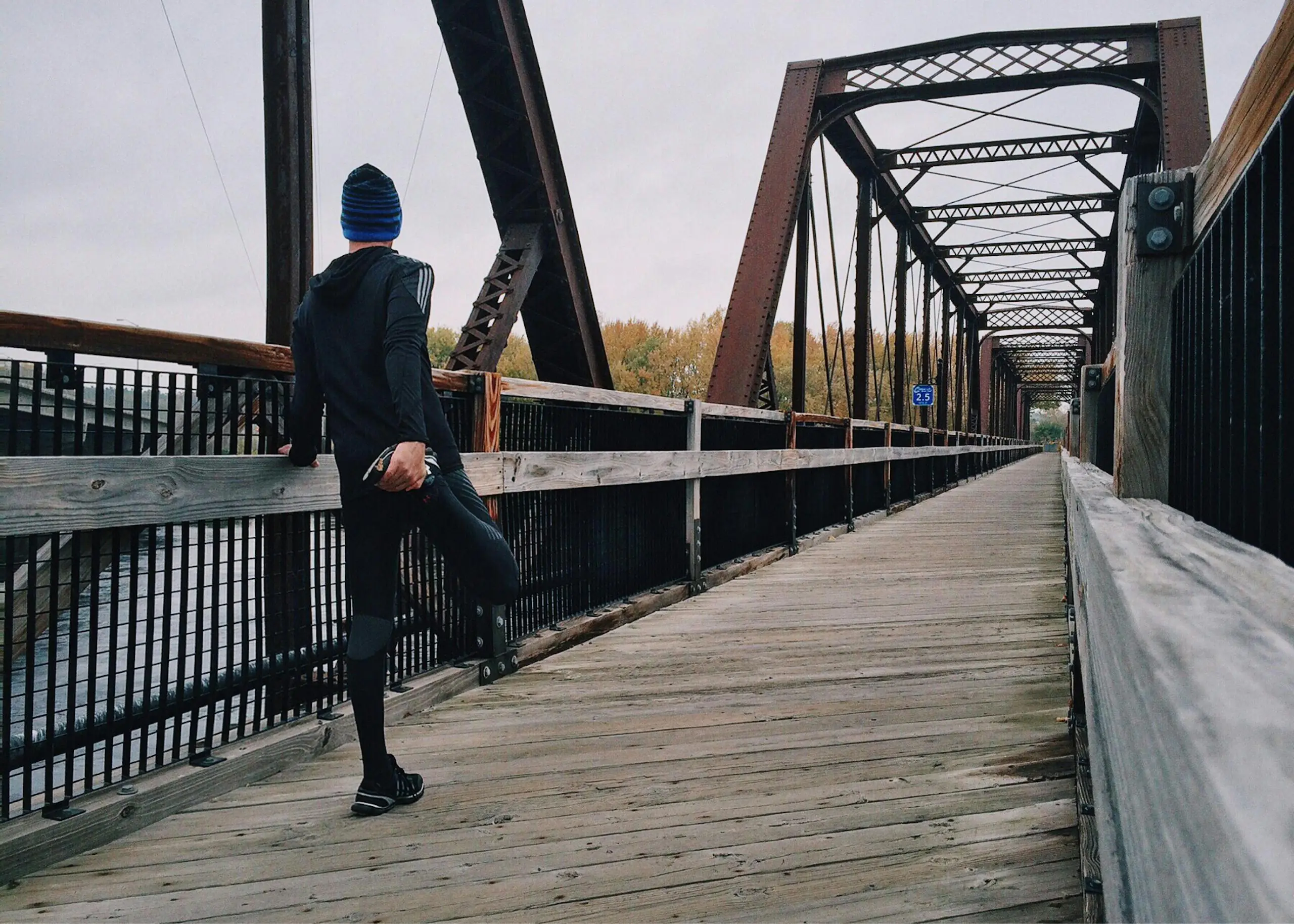Man stretching on wooden footbridge during daytime run emphasizing fitness recreation