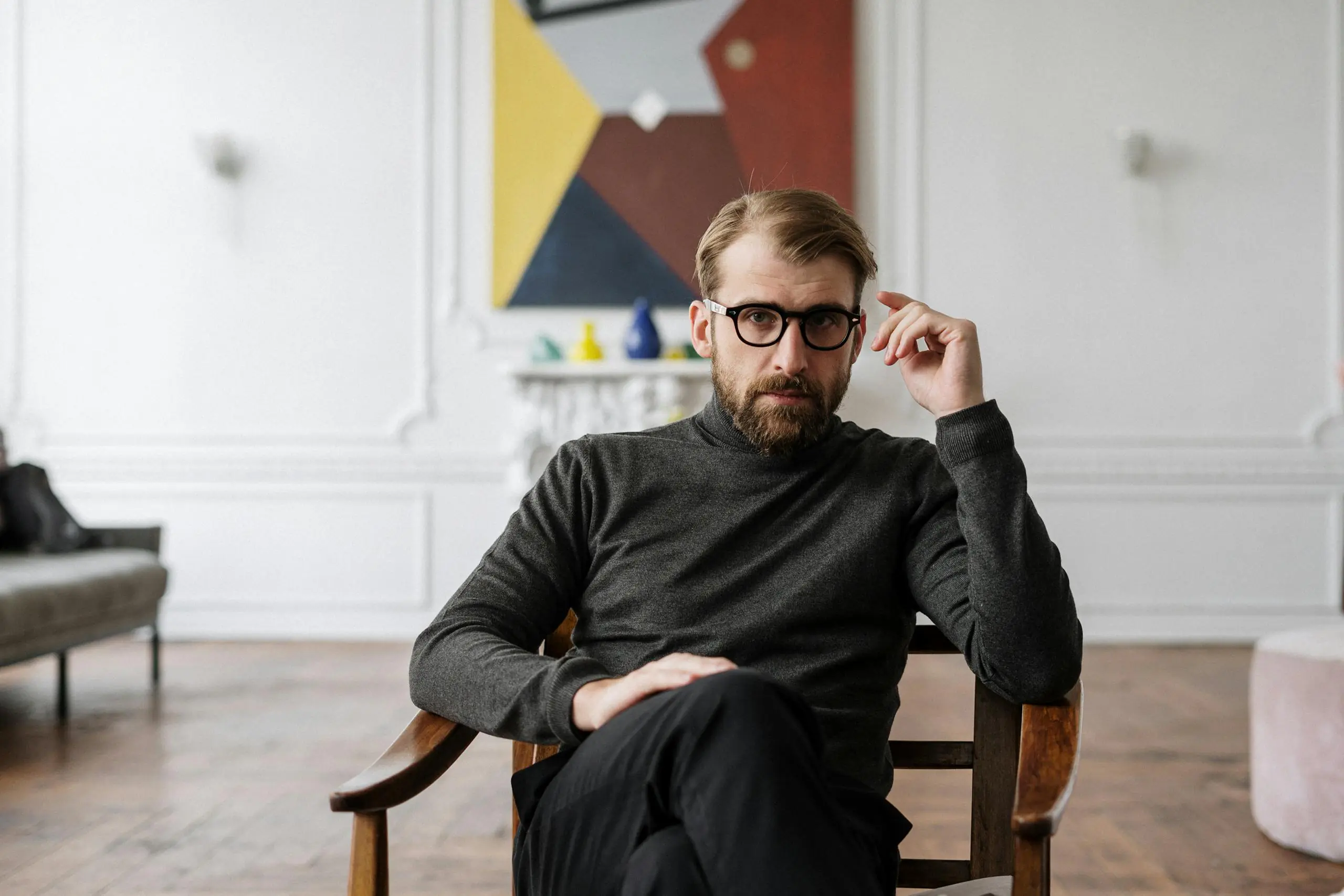 Man with glasses seated in modern interior space with abstract artwork.