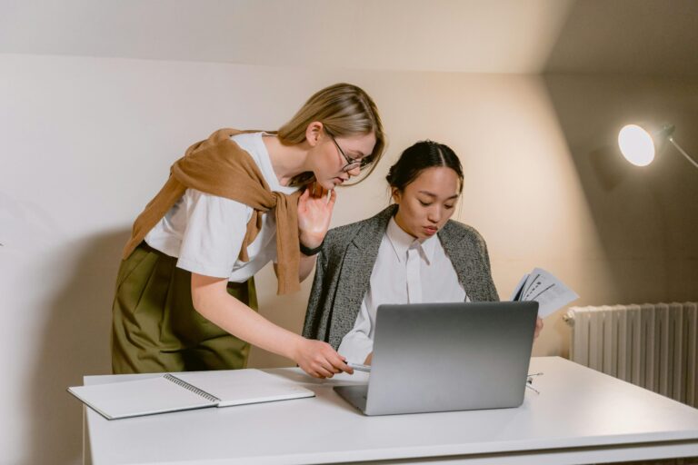 Two women collaborate on laptop at desk in bright minimalist office space