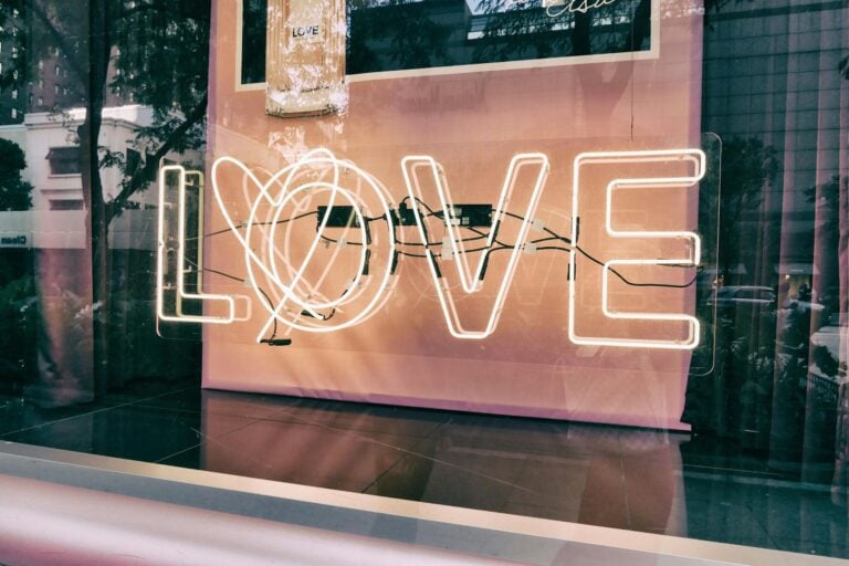 Neon love sign displayed in modern urban window with glass reflections.