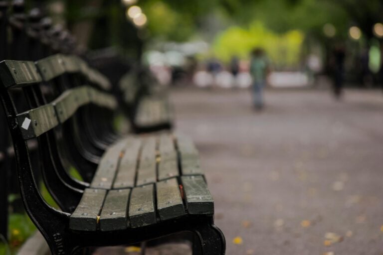 Empty park bench in focus with blurred people and green trees background