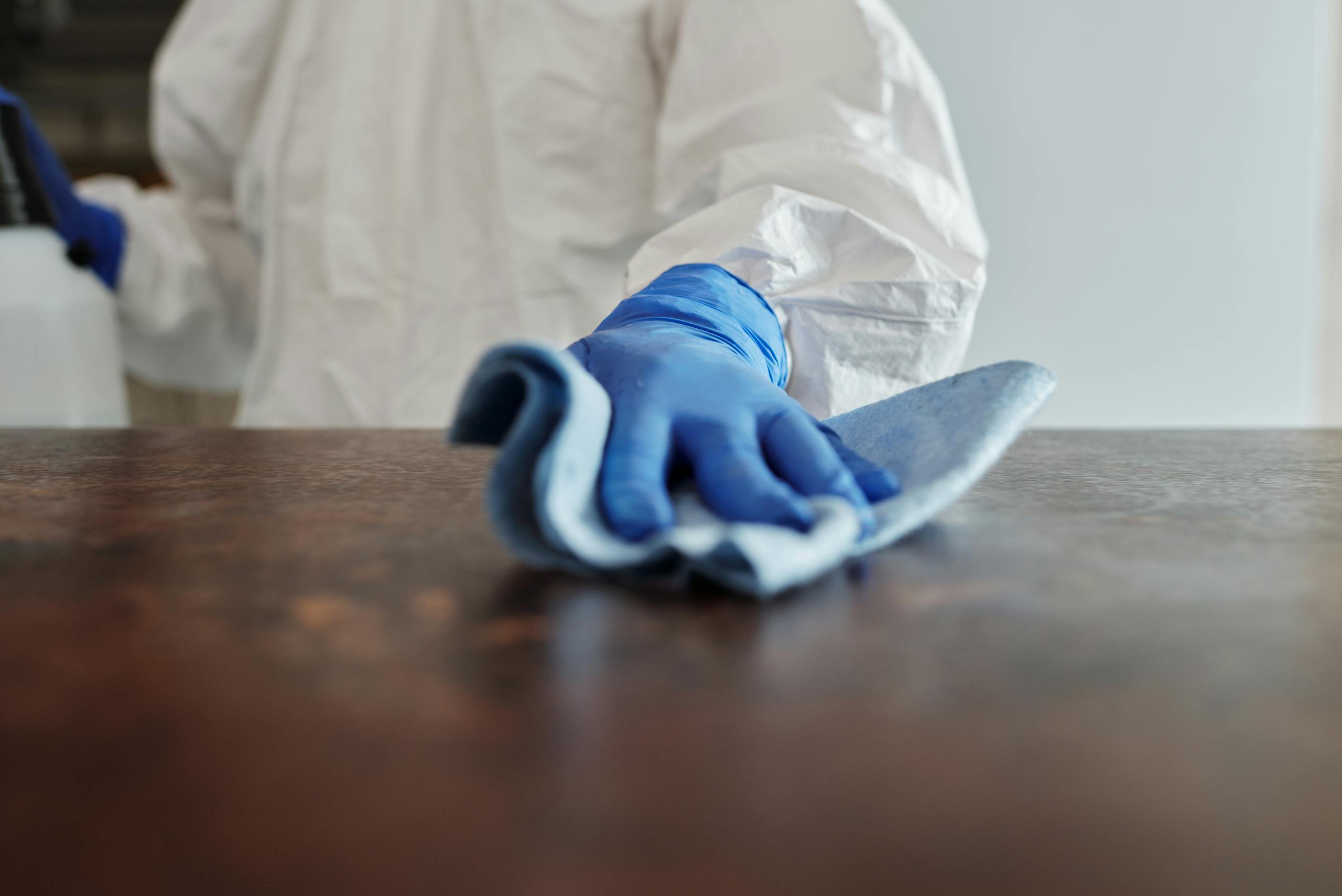 Person in protective suit using disinfectant on surface to ensure cleanliness and safety