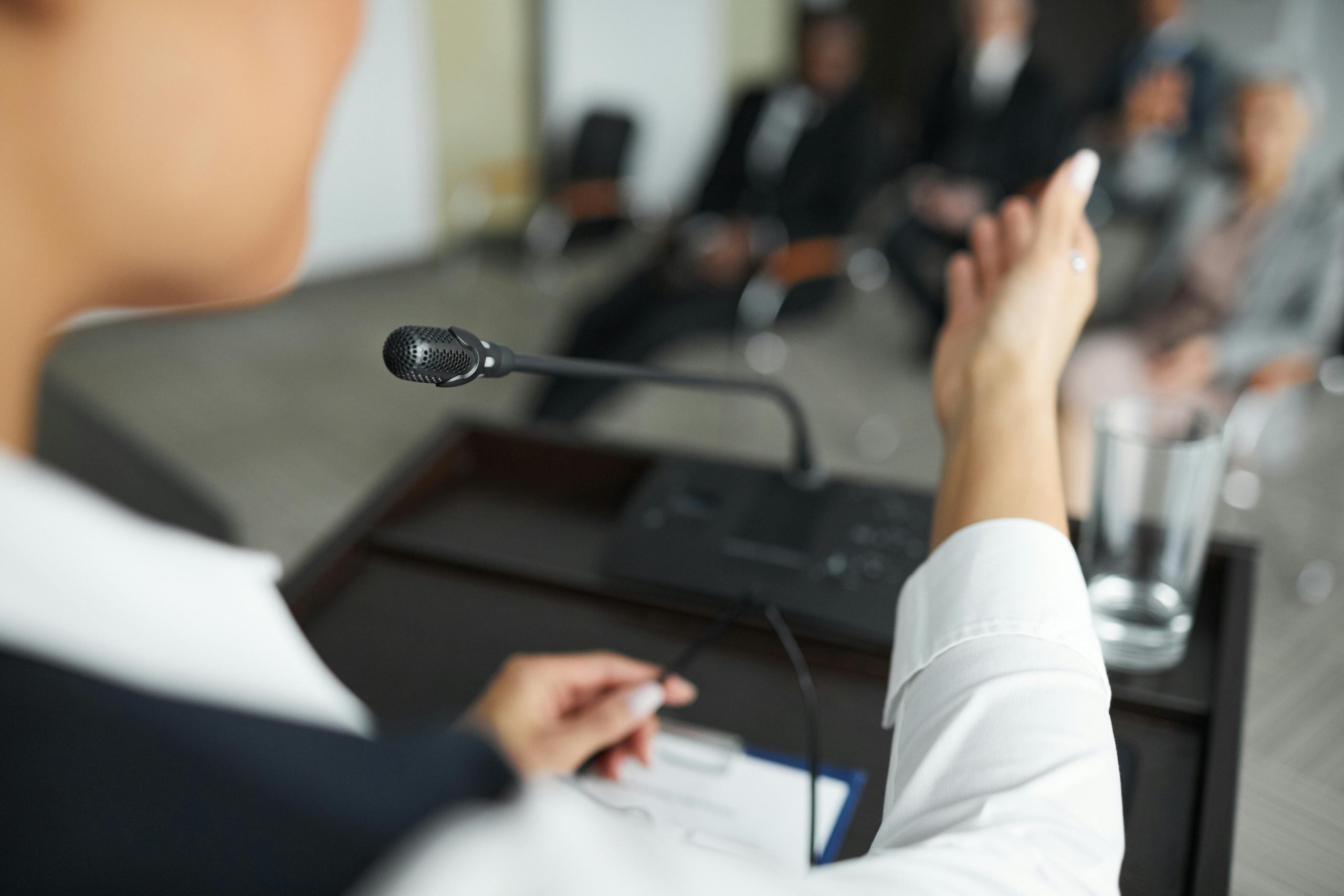 Professional woman speaking confidently at microphone during business presentation to audience