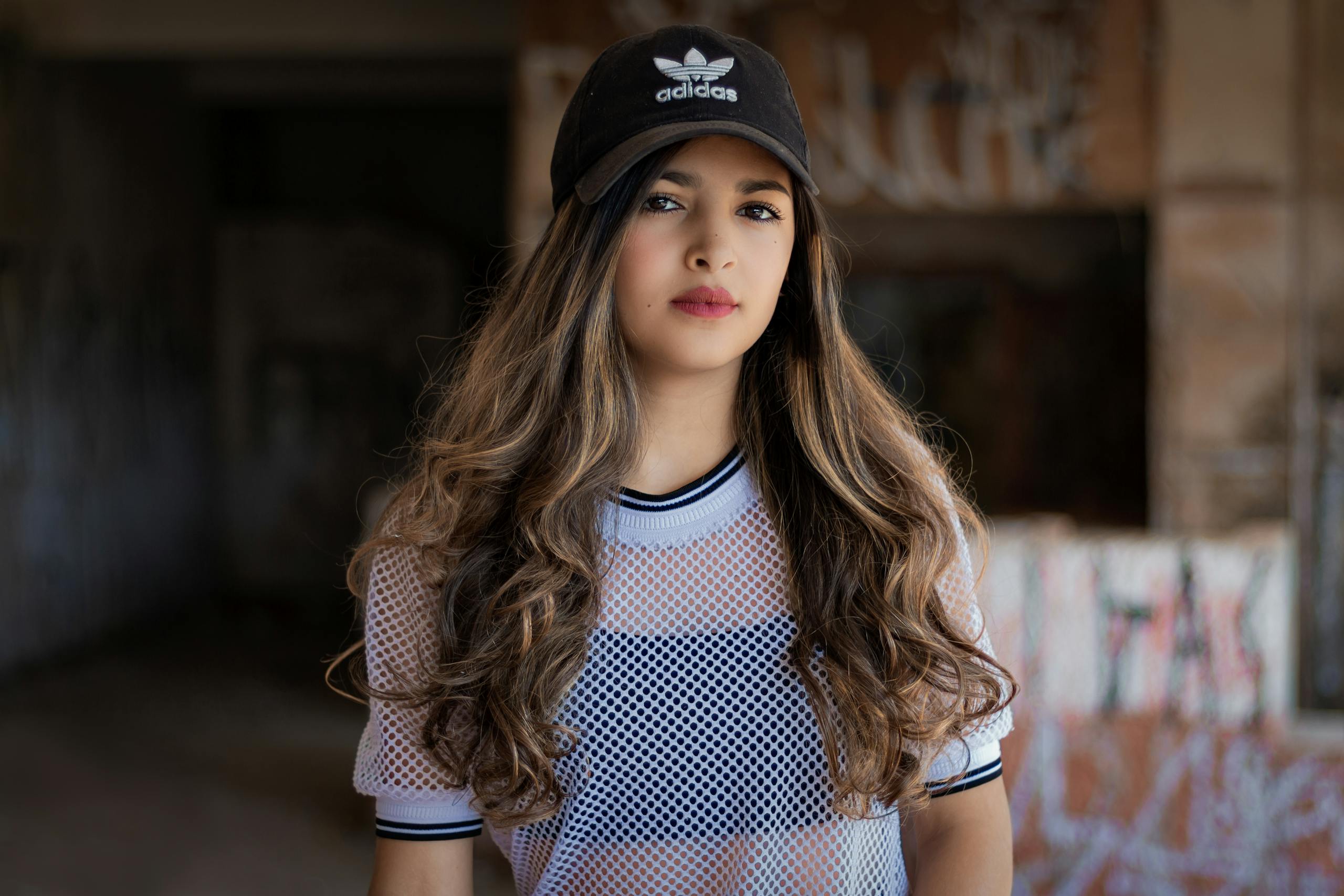 Portrait of young woman wearing Adidas cap and white mesh top.