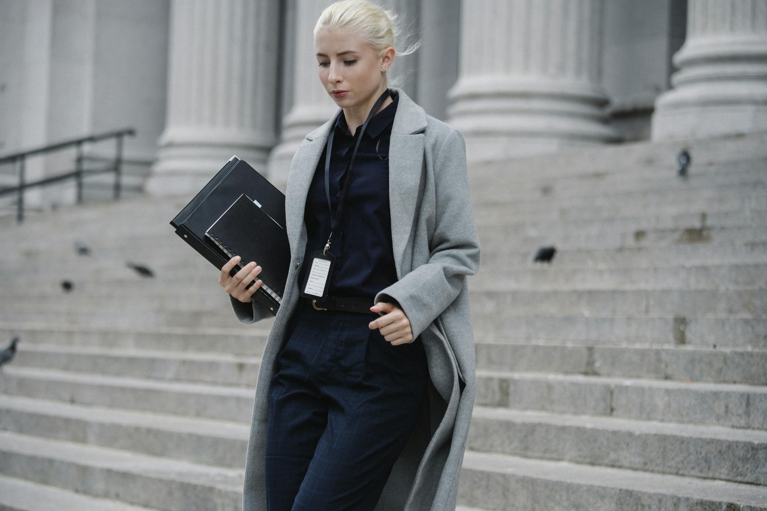 Professional woman in formal attire descending courthouse steps holding folders outdoors
