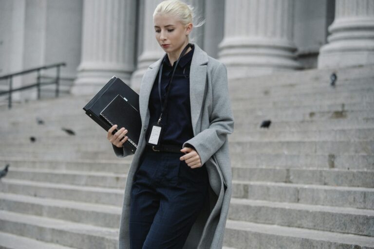 Professional woman in formal attire descending courthouse steps holding folders outdoors