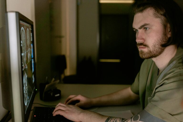 Radiologist intently studying CT scan results on computer monitor in healthcare setting.