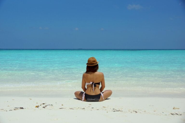 Woman in bikini and hat relaxing alone on pristine Maldives beach.