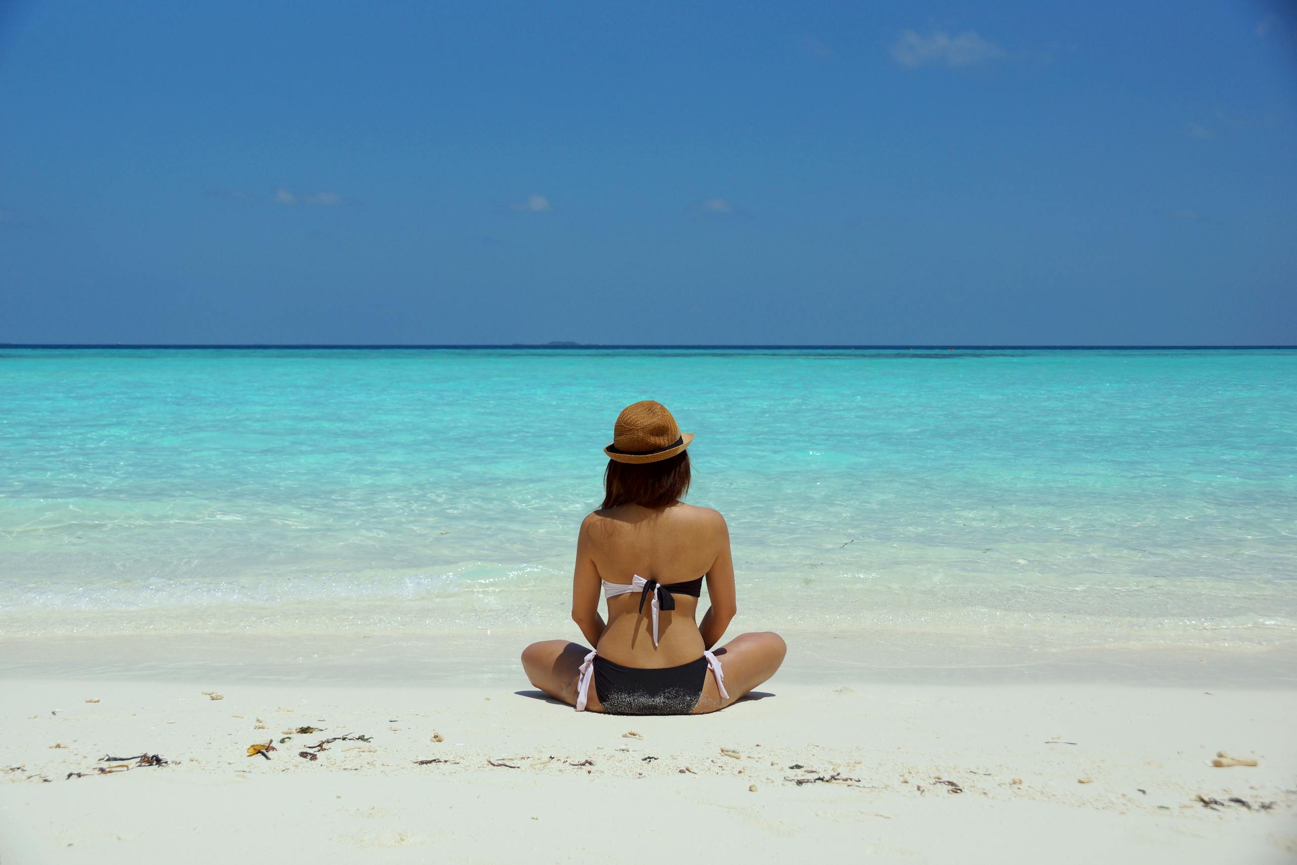 Woman in bikini and hat relaxing alone on pristine Maldives beach.