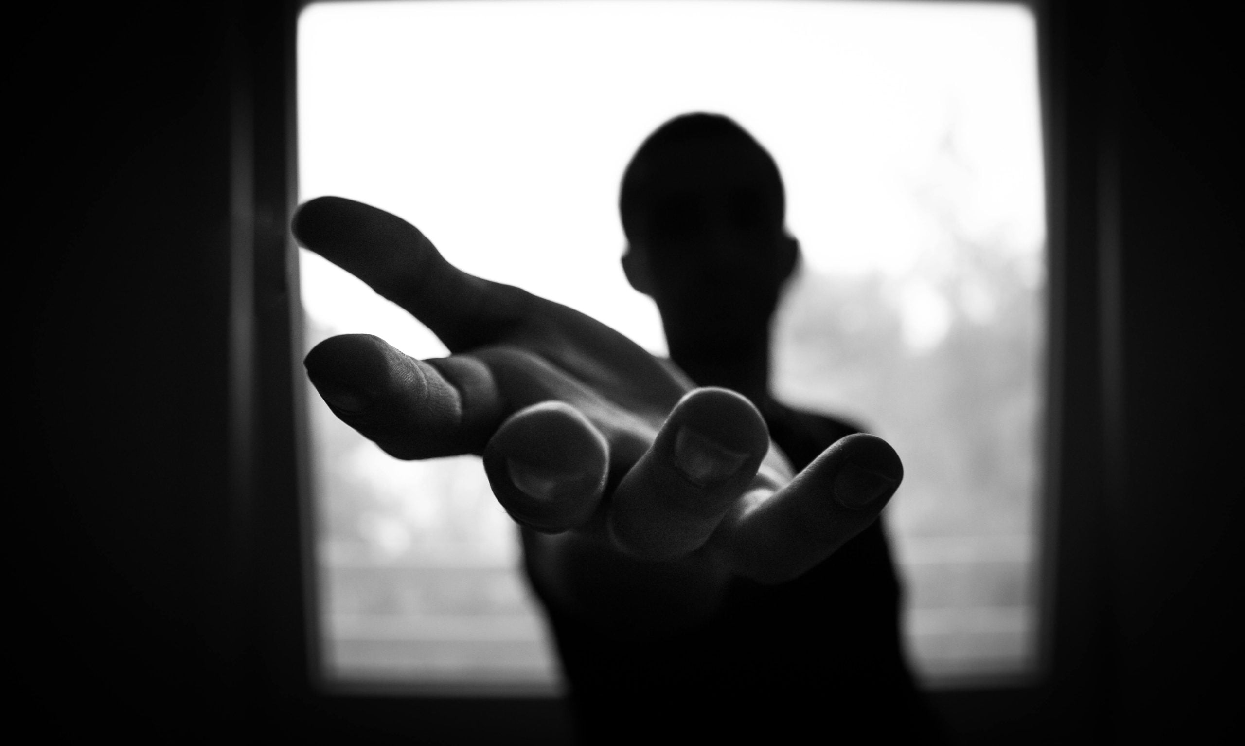 Silhouetted figure with outstretched hand reaching toward bright light window