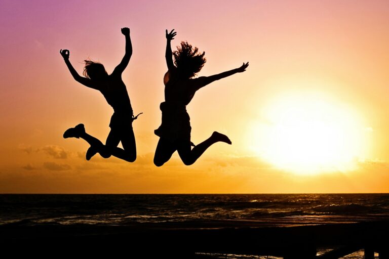 Silhouettes of two people joyfully jumping on beach during vibrant sunset.