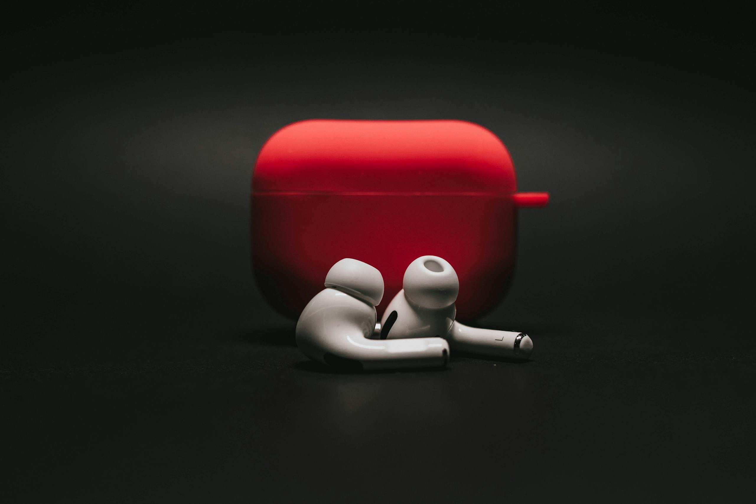 Sleek white earbuds with modern red case on dark surface stylishly.