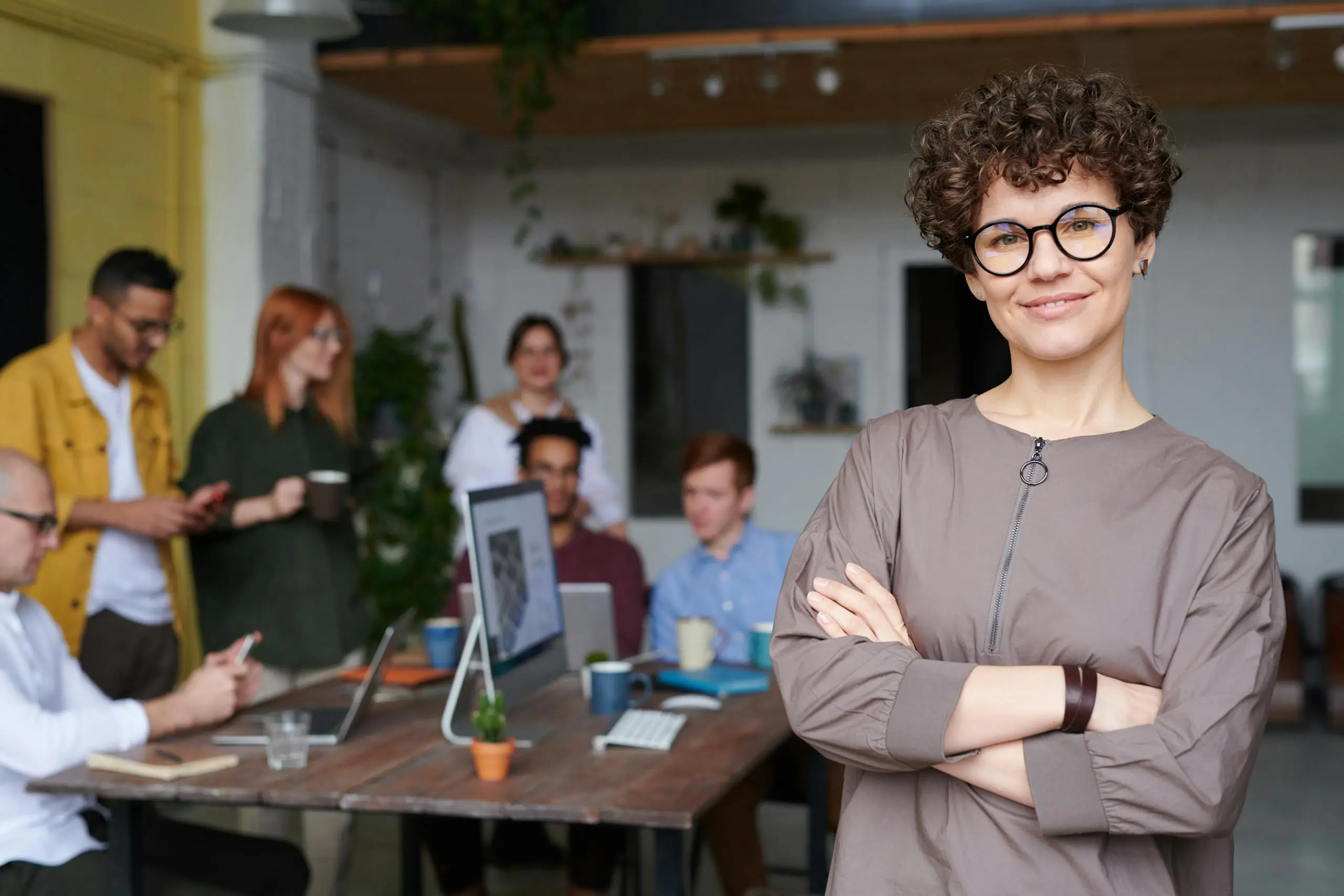 Smiling businesswoman with curly hair standing confidently in modern office.
