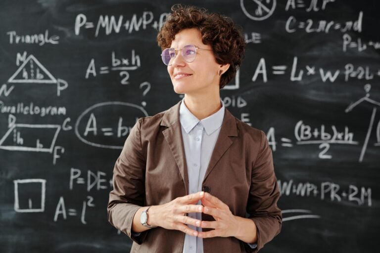Smiling female teacher standing before mathematical blackboard with complex equations.