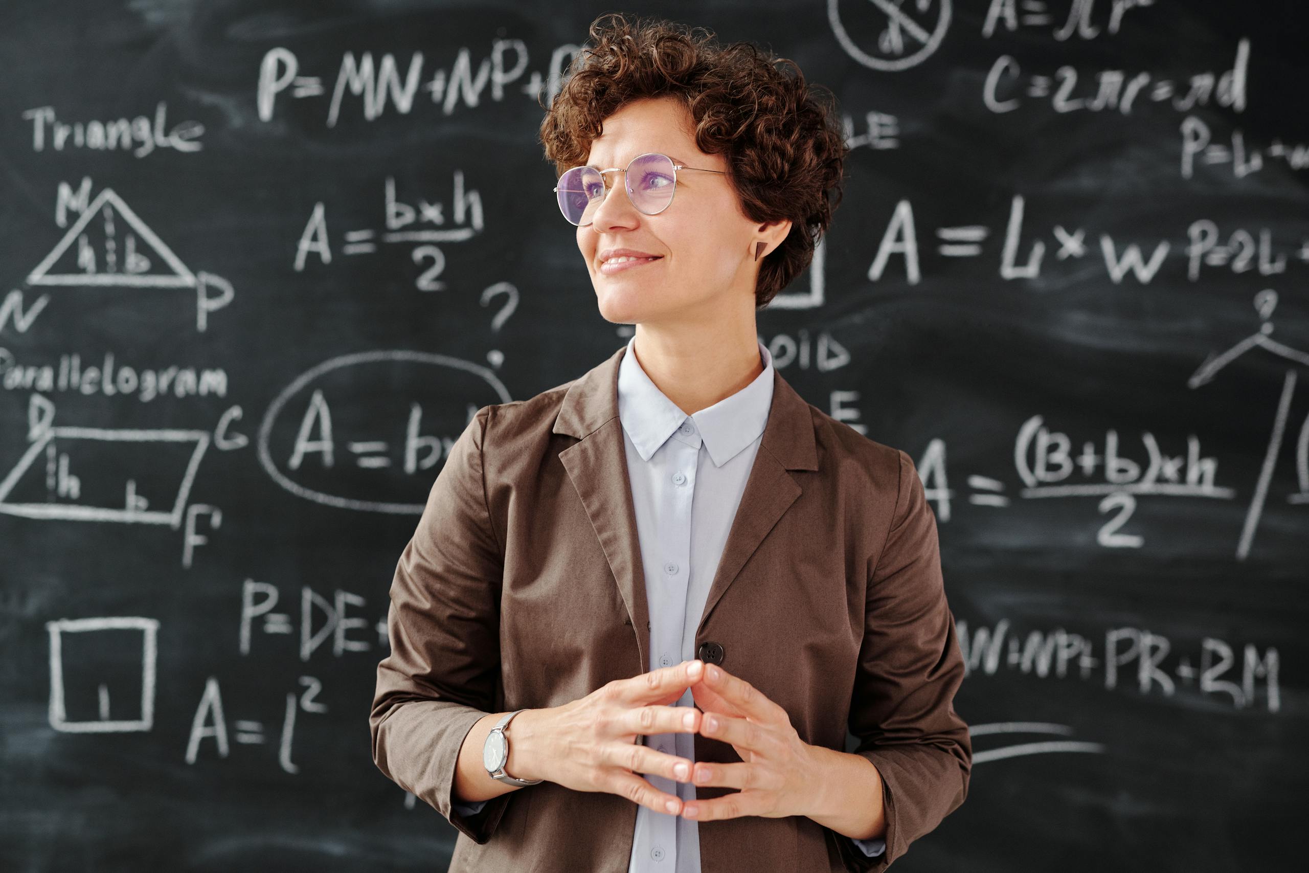 Smiling female teacher standing before mathematical blackboard with complex equations.