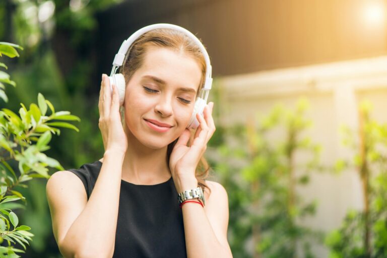 Smiling woman listening to music with headphones in sunny garden.
