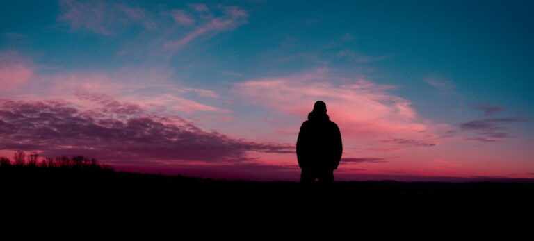 Solitary figure silhouetted against dramatic pink and purple sunset sky