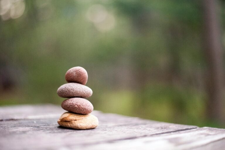 Stacked pebbles balanced carefully on wooden surface with blurred green nature background