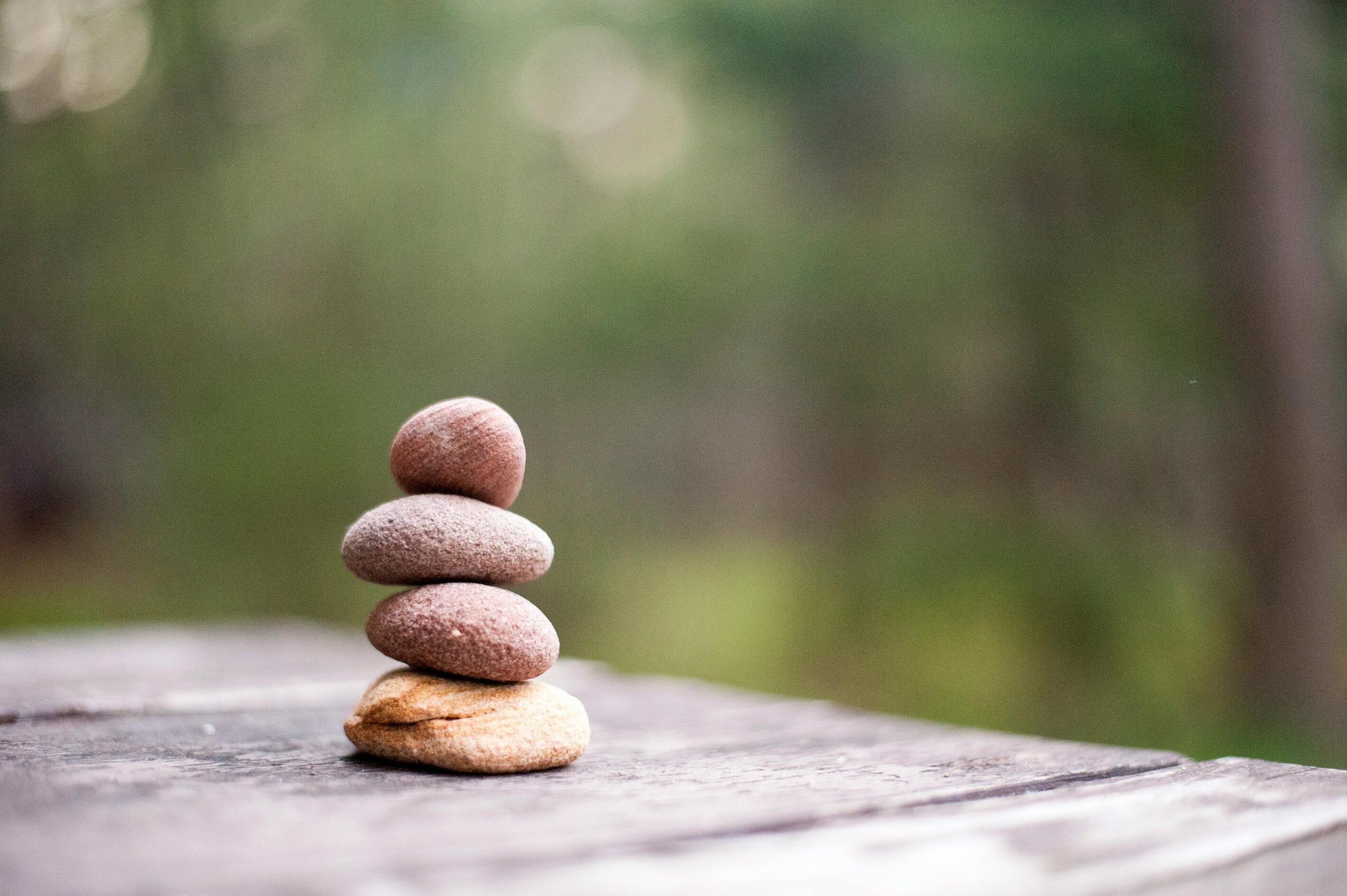 Stacked pebbles balanced carefully on wooden surface with blurred green nature background