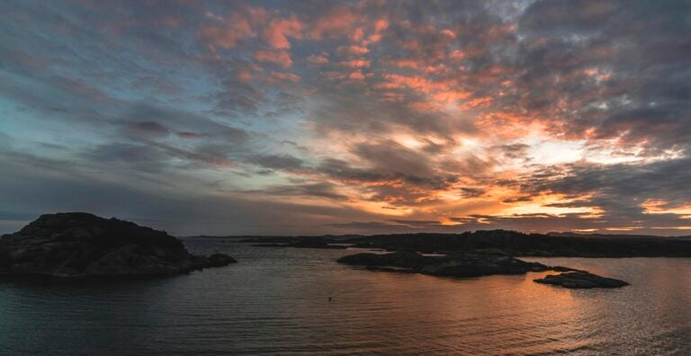 Scenic sunset with colorful sky and clouds over calm ocean and rocky shoreline