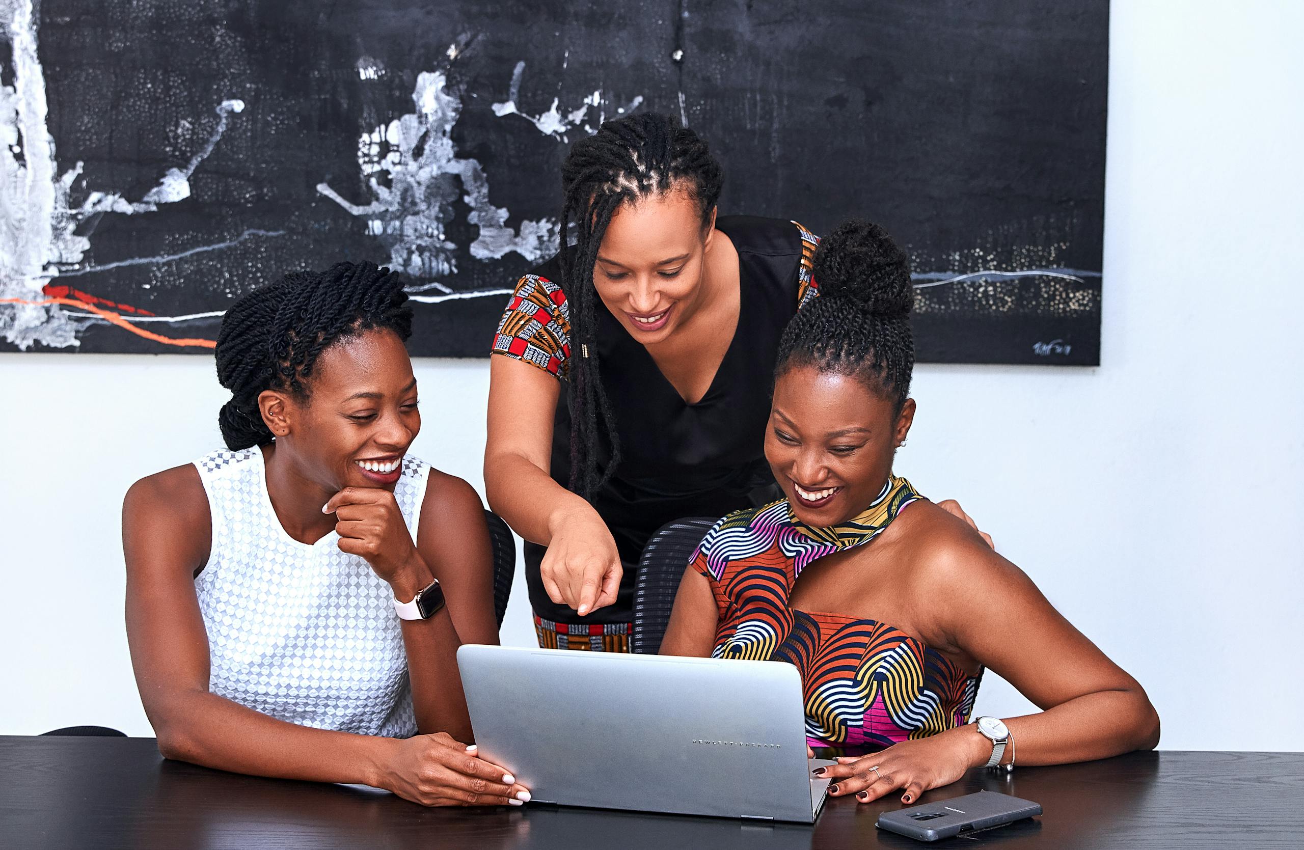 Three African American women collaborating happily at laptop during meeting.