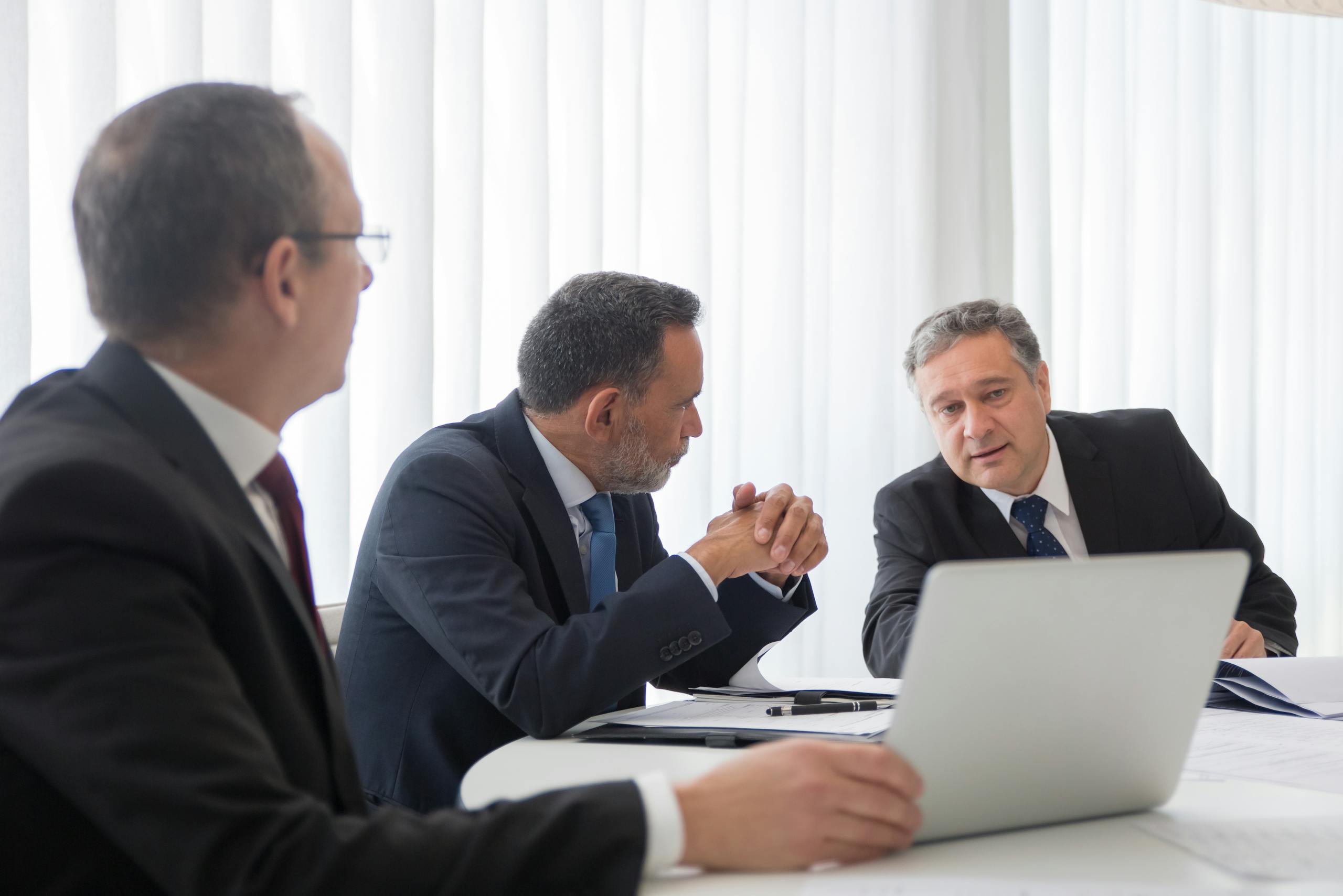Three businessmen collaborating around laptop during bright office meeting