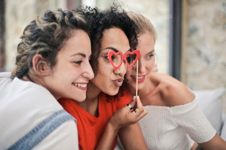 Three women wearing heart-shaped glasses enjoying playful moment together