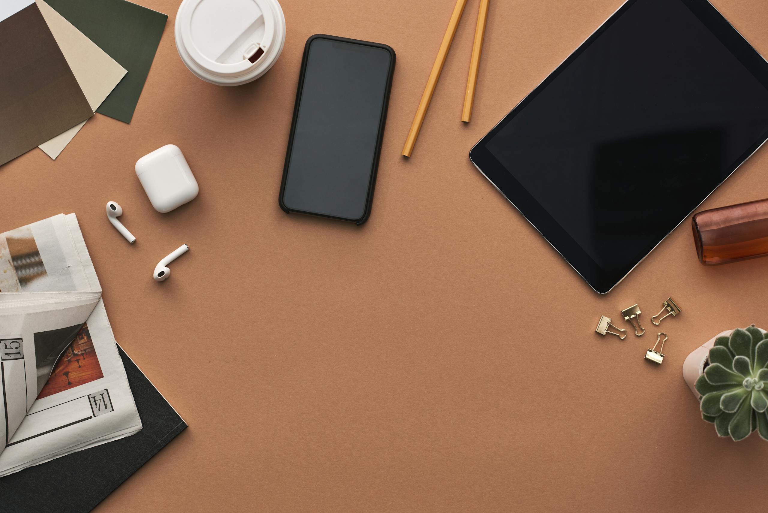 Organized workspace with technology gadgets and stationery on brown background.