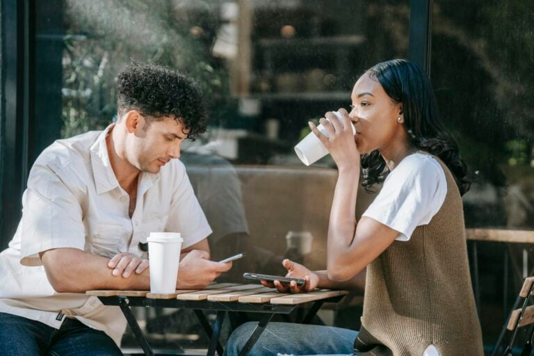 Two friends enjoying casual coffee break outdoors with smartphones in close-up view