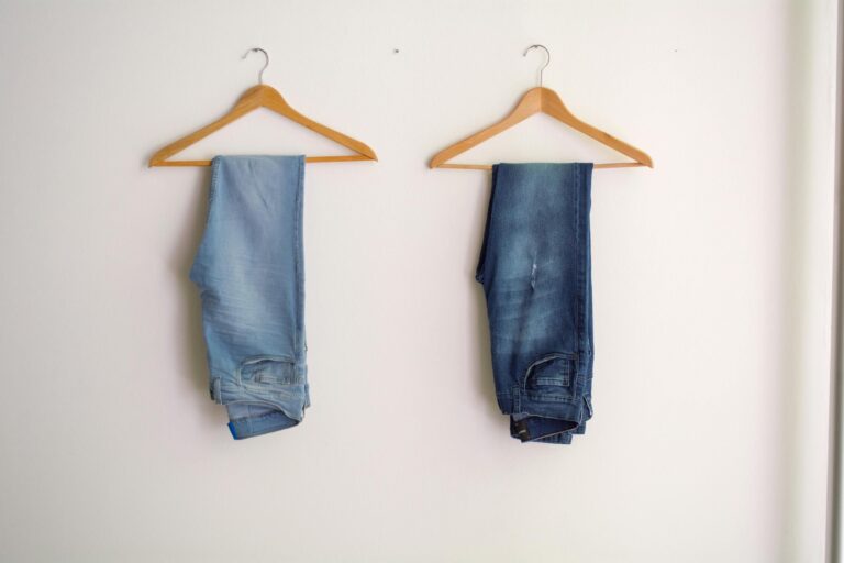 Two pairs of blue denim jeans hanging neatly on wooden hangers