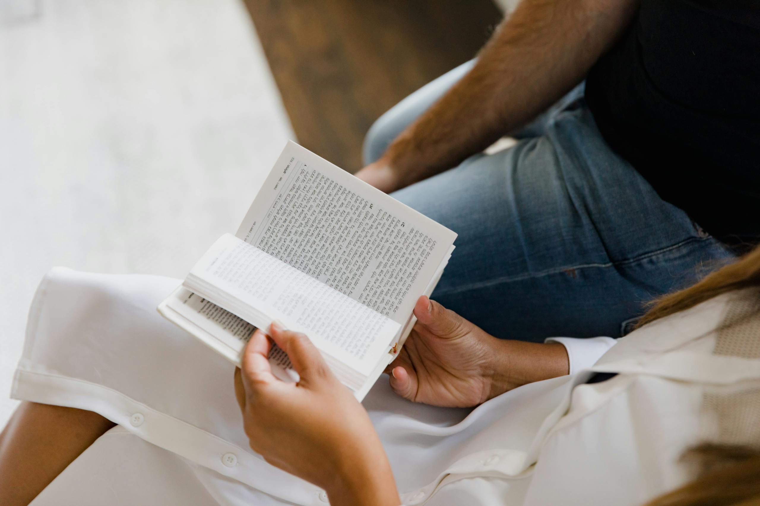 Two people reading book together indoors, one in white dress