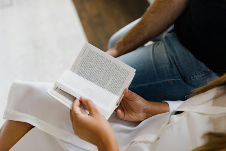Two people reading book together indoors, one in white dress