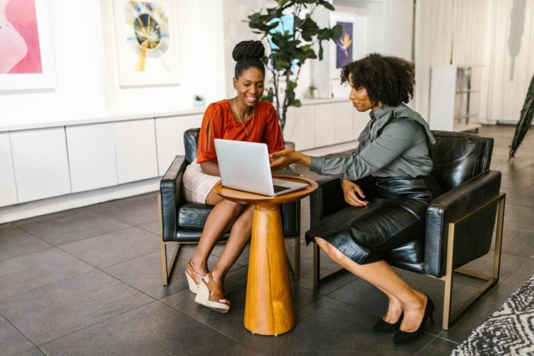 Two professional women collaborating on laptop project in modern office setting