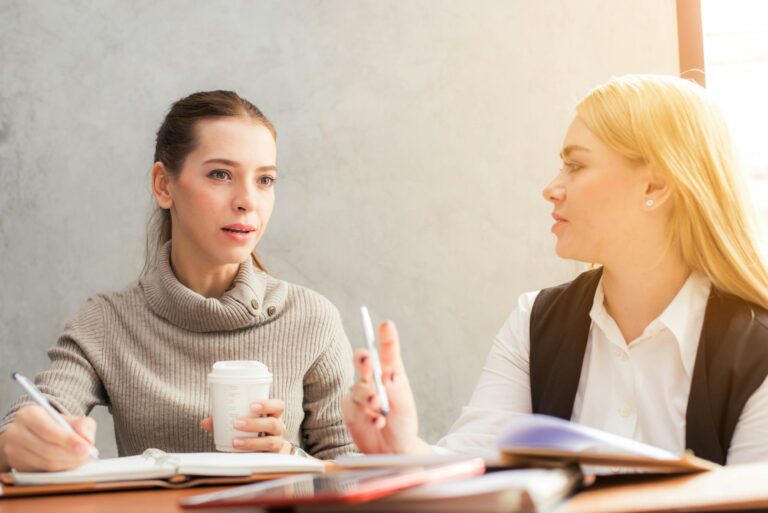 Two women engaging in professional conversation over coffee and notes.
