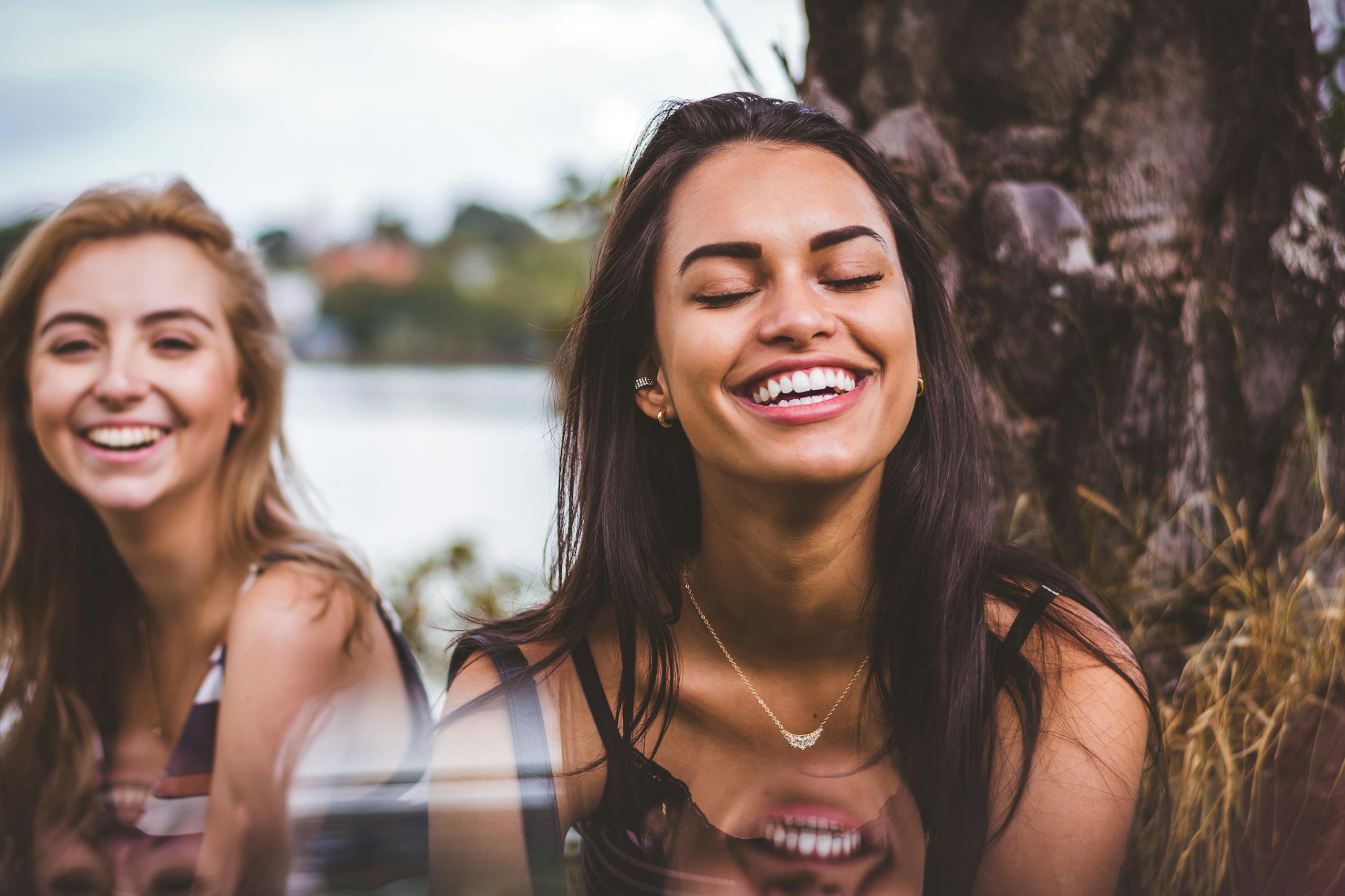 Two women happily laughing together outdoors by serene lakeside
