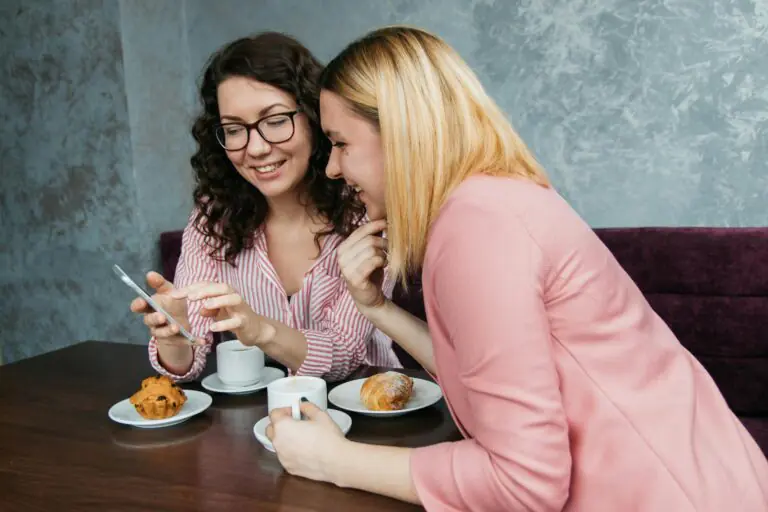 Two women laughing together over coffee and pastries in cozy setting